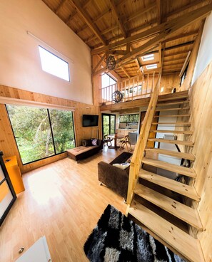Amplia sala de estar con escalera de madera, ventanas grandes y un rincón de estar acogedor.