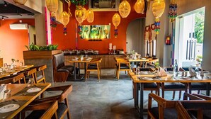 A restaurant with wooden tables and chairs, hanging wicker lamps, and a colorful wall decoration. - UDICHI REGENCY (Bolpur)