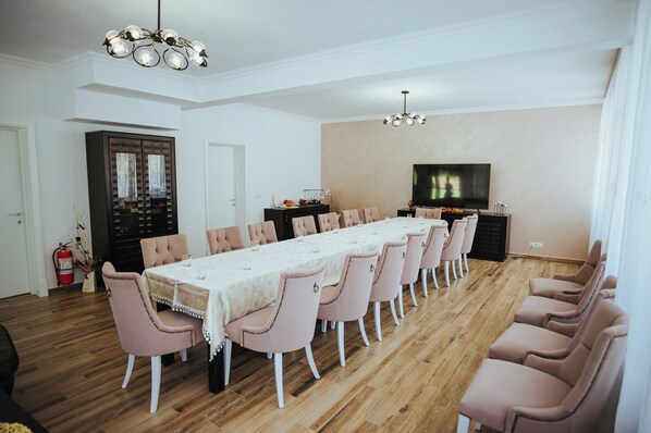 A dining room with a long table, pink chairs, and a television on the wall. - Baile Puturoasa (Vama)