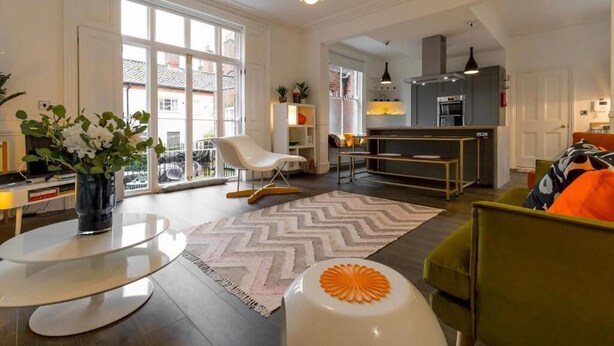 Una sala moderna con una mesa de comedor, un sofá y una cocina al fondo.