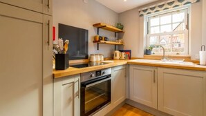 A kitchen with white cabinets, a wooden countertop, a built-in oven, and a window with a view of a house.