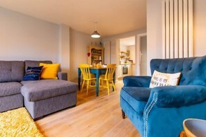 Ein Wohnzimmer mit einer Couch, einem blauen Sessel und einem Esstisch mit Stühlen.