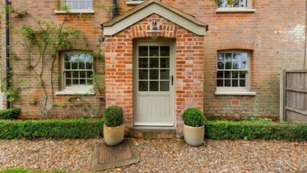A brick building with a central entrance, two potted plants on either side, and a small garden area with mulch. - Host & Stay | Haclins Cottage (Stibbard)