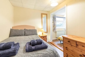 A bedroom with a bed, a wooden dresser, a nightstand with a lamp, and a window with curtains. - Host & Stay | Wylaway (Norwich)