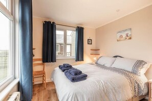 Una camera da letto con un letto, una finestra con tende, una sedia e un quadro appeso al muro.
