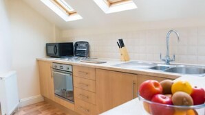 Una cocina con microondas, cafetera y un cuenco de fruta en la encimera.