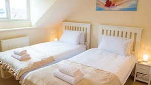 Un dormitorio con dos camas individuales, un radiador, una mesita de noche con lámpara y un cuadro en la pared.