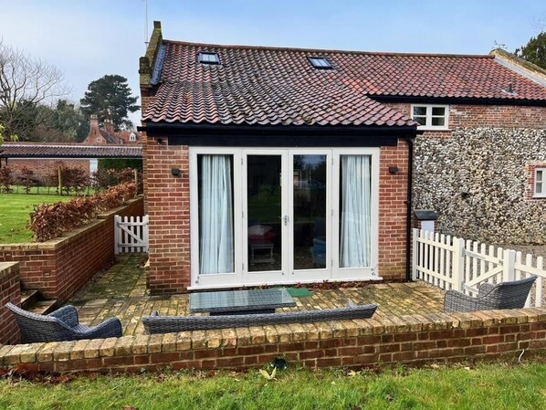 A brick house with a tiled roof, a glass door, and a small patio with wicker furniture.