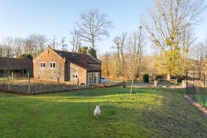 A brick house with a sloped roof, a fenced yard, and a small pond.