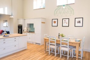 A modern kitchen with white cabinets, a wooden dining table, and a hanging light fixture.