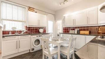 A modern kitchen with white cabinets, a washing machine, and a dining area with white chairs.