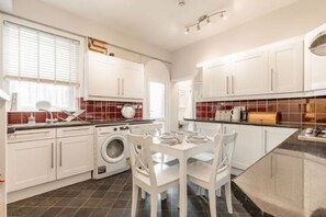 A modern kitchen with white cabinets, a washing machine, and a dining area with white chairs. - Host & Stay | Cromer Town, Apartment 1 (Cromer)