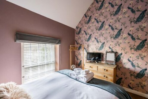 Une chambre à coucher comprenant un lit, une commode, un téléviseur et une fenêtre avec des stores.