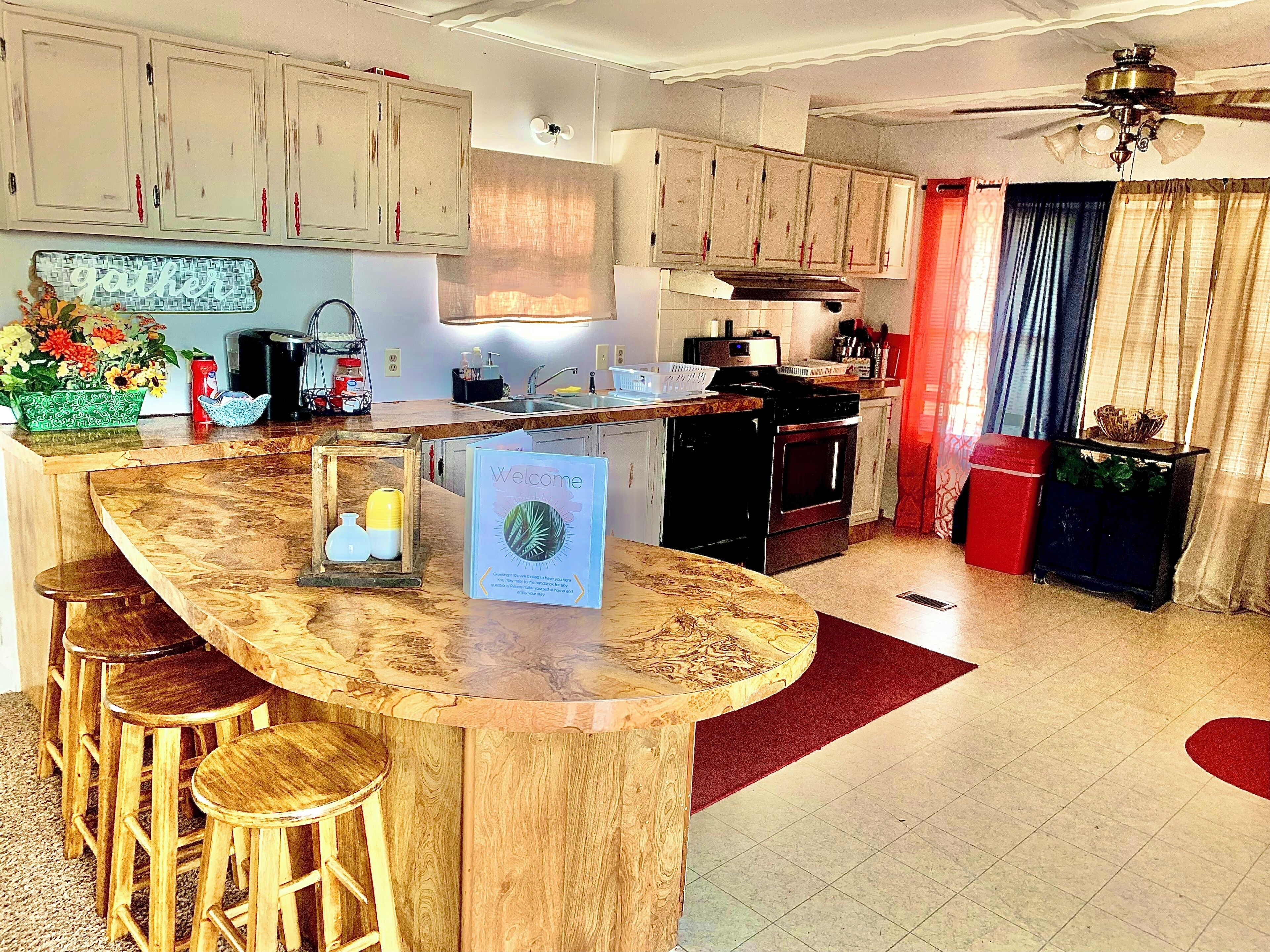 A kitchen with wooden cabinets, a central island with stools, a ceiling fan, and a welcome sign.