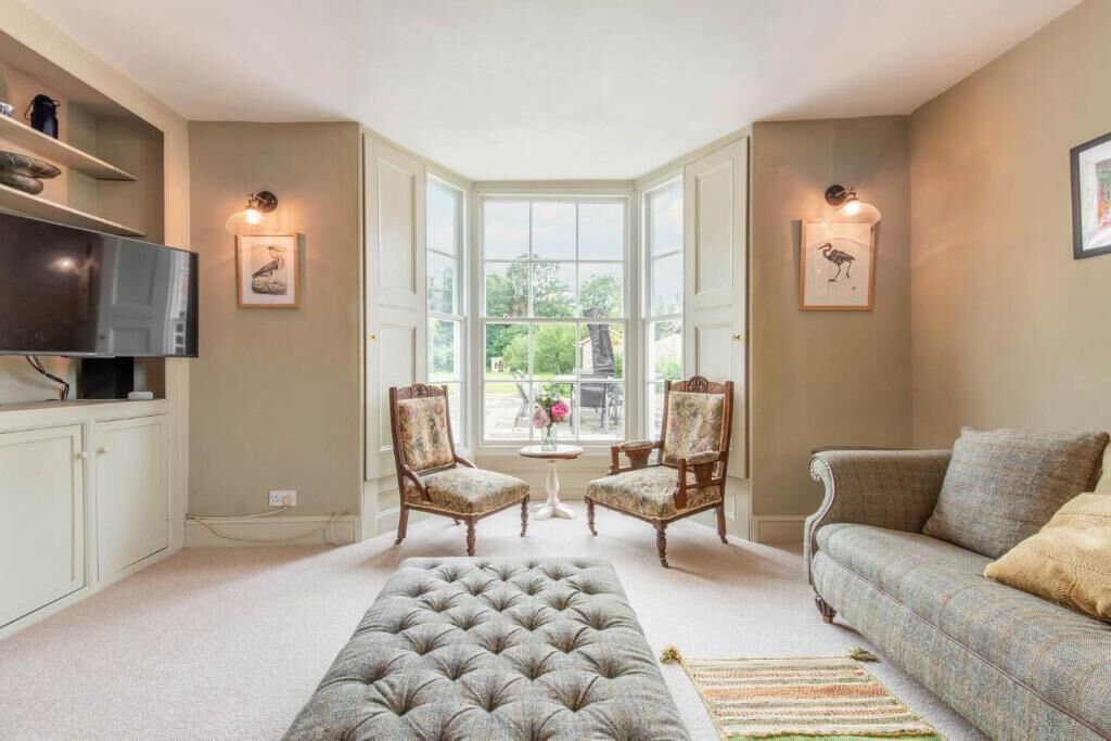 Un salon avec une grande fenêtre, deux fauteuils, un canapé, un téléviseur et un tapis décoratif.