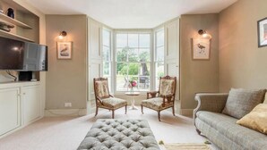 A living room with a large window, two armchairs, a sofa, a television, and a decorative rug. - Host & Stay | Mill House (Worthing)