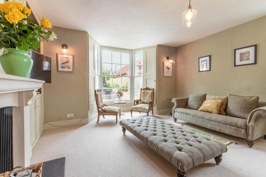 A cozy living room with a fireplace, a sofa, an ottoman, and a dining area with chairs.