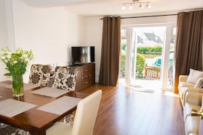 A living room with a dining table, sofa, TV, and a view of the outside.
