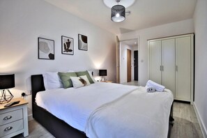 A modern bedroom with a large bed, bedside tables, a wardrobe, and framed artwork on the wall. - Manchester - 2-bed Apartment - Sleeps 4 - Wifi (Salford)