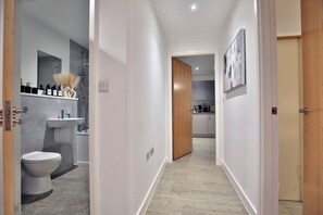 A modern bathroom with a toilet, sink, and shower. A hallway leads to a kitchen area. - Manchester - 2-bed Apartment - Sleeps 4 - Wifi (Salford)