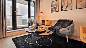 En moderne stue med sofa, sofabord og et stort vindue med gardiner.