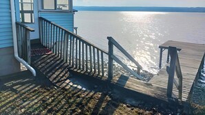 A wooden dock leading to a house with a blue exterior and a view of a calm body of water.