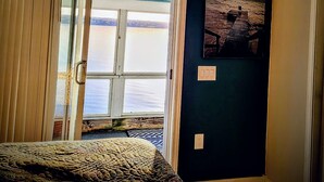 A bedroom with a large window, a bed, and a painting of a beach scene.