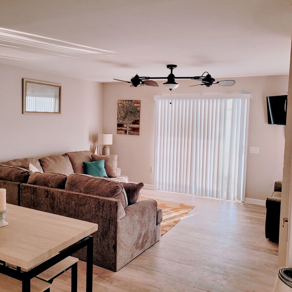 Ein Wohnzimmer mit einer Couch, einem Esstisch, einer Lampe und einem Deckenventilator.
