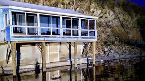 A waterfront house with a balcony overlooking a body of water, supported by wooden stilts.