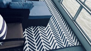A modern, nautical-themed interior with a large window overlooking a body of water, a sofa set, and a patterned rug.