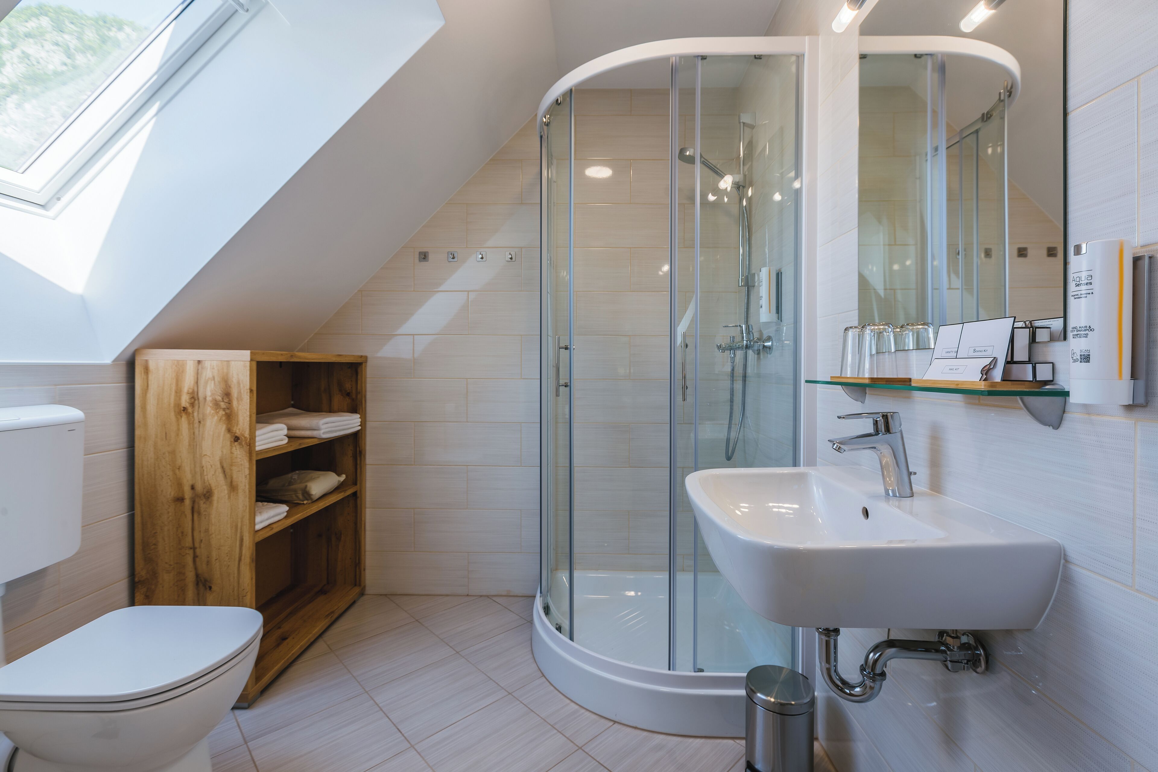 A modern bathroom with a glass-enclosed shower, a white sink, and a wooden shelf unit.