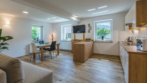 Een moderne keuken met houten kastjes, een eethoek met een tafel en stoelen, en een groot raam met uitzicht op de omgeving.