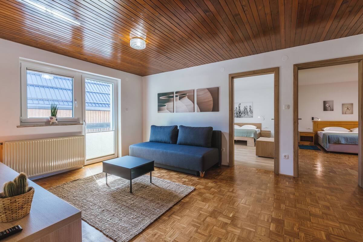 Een moderne woonkamer met een houten plafond, een bank, een salontafel en uitzicht op het exterieur door grote ramen.