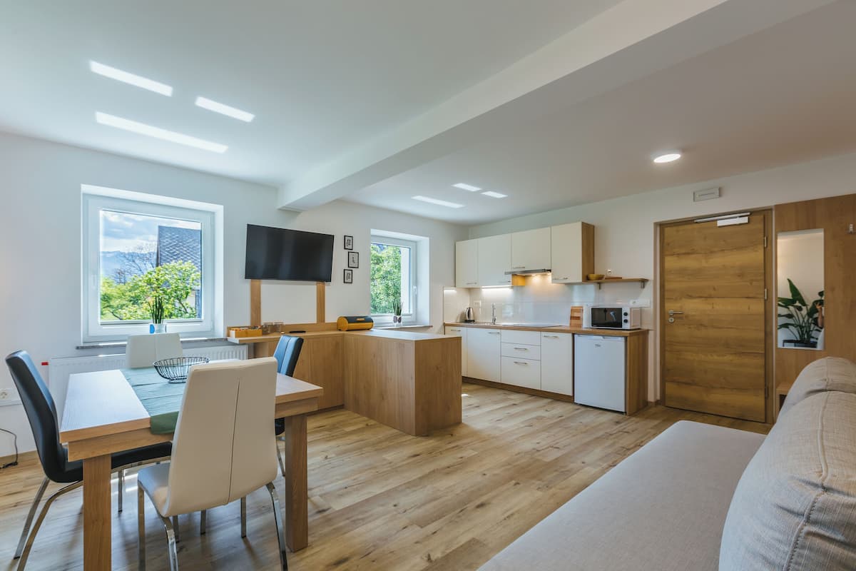 Een moderne keuken met houten kastjes, een zithoek met een tafel en stoelen, en een groot raam dat voor natuurlijk licht zorgt.