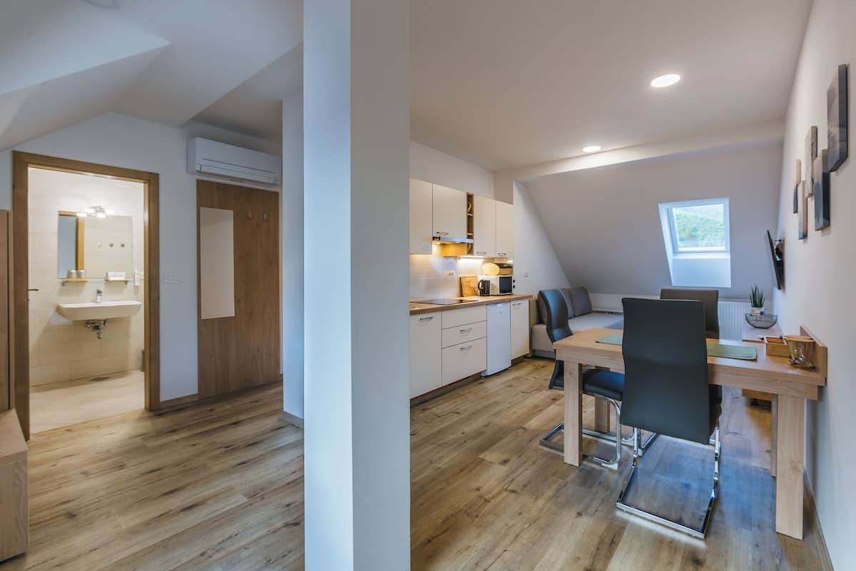 Een moderne keuken met houten kastjes, een eethoek met een tafel en stoelen, en een klein raam dat voor daglicht zorgt.