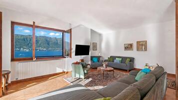 A living room with a large window, a flat-screen TV, a sofa, a coffee table, and a view of a mountainous landscape.