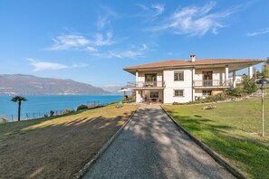 A two-story house with a balcony, a paved driveway, and a view of the sea. - Casa Antonia: Lake Maggiore Villa With Private Pool (Porto Valtravaglia)
