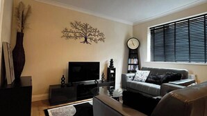 A modern living room with a sofa, a coffee table, a TV, and a decorative tree wall art piece. - Durham, 3-beds, Sleeps 5 - Close to Uni & Centre (Durham)