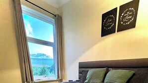 A neatly made bed with a green quilt, a rolled white towel, and a folded beige towel. There are two pillows on the bed, one green and one brown. A window with curtains is visible, and two framed quotes are on the wall. - Durham, 3-beds, Sleeps 5 - Close to Uni & Centre (Durham)
