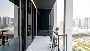 A modern balcony with a city view, a glass door, and a small table with stools. - Cozy Studio w/ Burj View Balcony, Business Bay (Dubai)