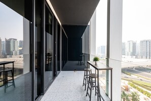 A modern balcony with a city view, a glass door, and a small table with stools.