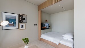 A modern bedroom with a bed, a TV mounted on the wall, and framed artwork on the wall. - Cozy Studio w/ Burj View Balcony, Business Bay (Dubai)