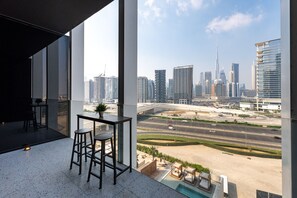 A modern room with a city view, a dining area with stools, and a small table with a plant. - Cozy Studio w/ Burj View Balcony, Business Bay (Dubai)
