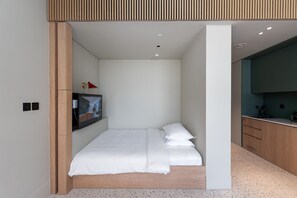 A modern bedroom with a bed, a TV, and a kitchenette. - Cozy Studio w/ Burj View Balcony, Business Bay (Dubai)