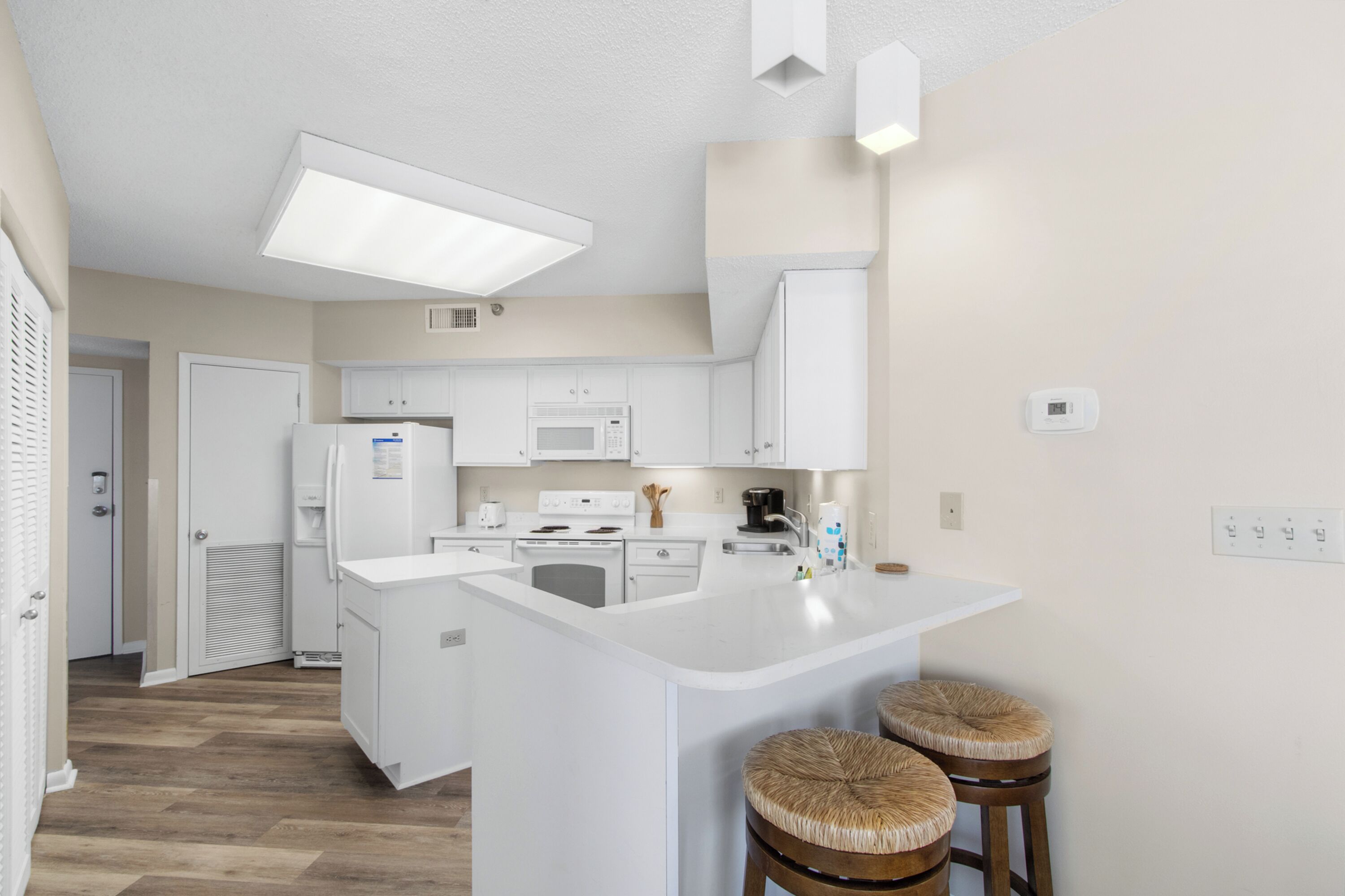A modern kitchen with white cabinetry, a central island with stools, a microwave, and a coffee maker.