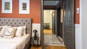 A bedroom with a tufted headboard, a bed with white bedding, a small side table with a lamp, and two framed artworks on the wall. - Vintage Acropolis Retreat: Charming 3-Bdrm in Koukaki (Athens)