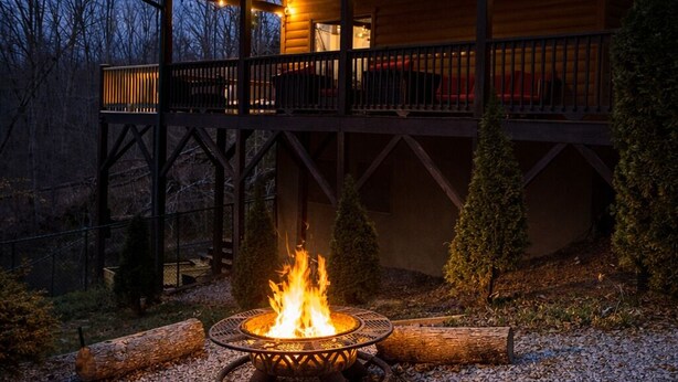 Una cabaña de troncos con una chimenea, un pozo de fuego y una terraza de madera.