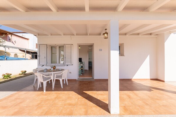 A covered patio with a table and chairs, a tiled floor, and a view of a building with a balcony. - Apartments In Golfo Orosei (Orosei)