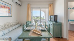 A dining area with a table set for four, a sofa, a television, and a view of the outdoors. - Apartments In Golfo Orosei (Orosei)