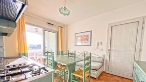 A kitchen with a gas stove, a dining table with chairs, a bench, and a door. - Apartments In Golfo Orosei (Orosei)